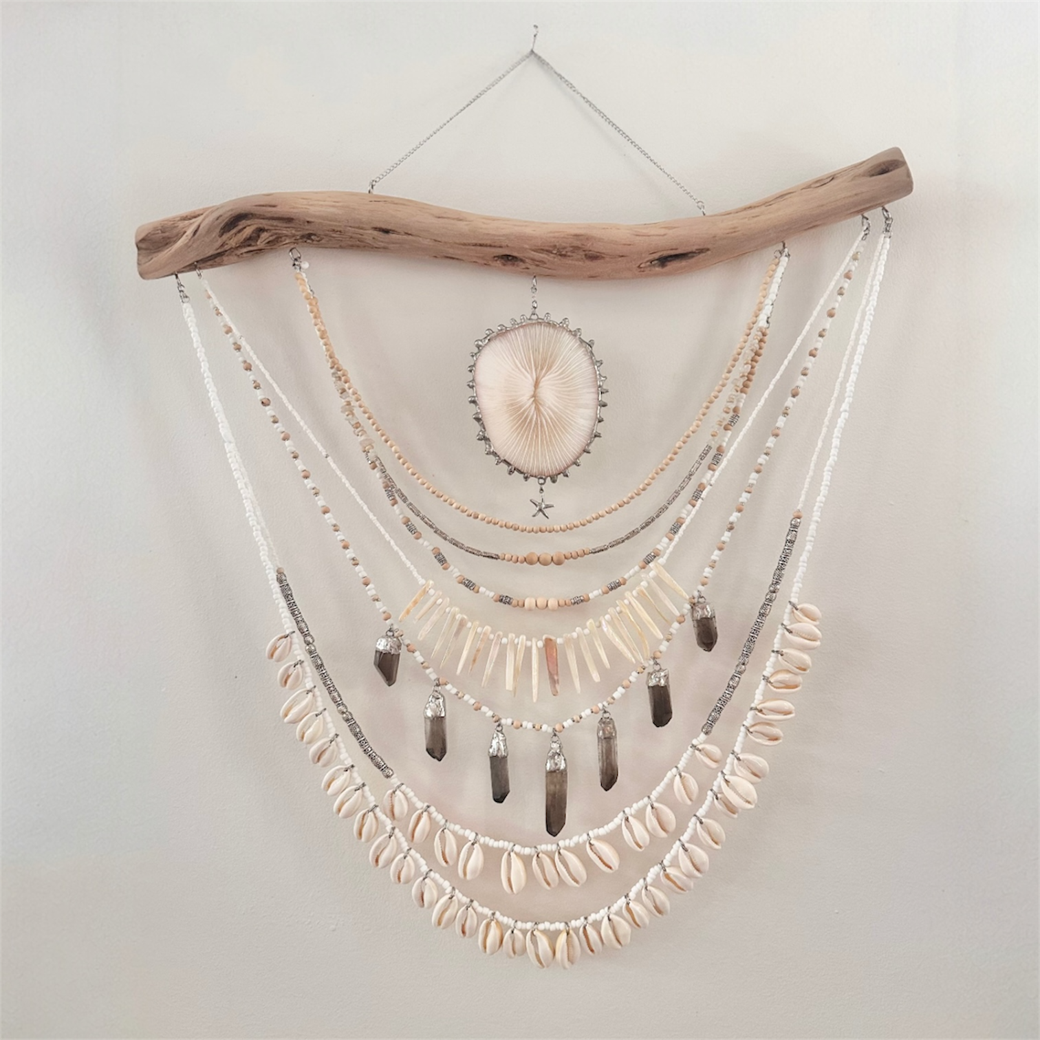 Decorative wall hanging with shells, beads, and a piece of driftwood on a light background