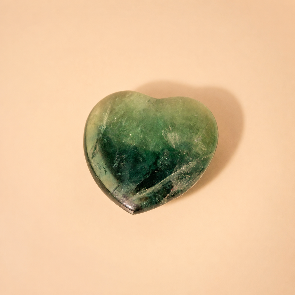 Heart-shaped green fluorite crystal on a beige background