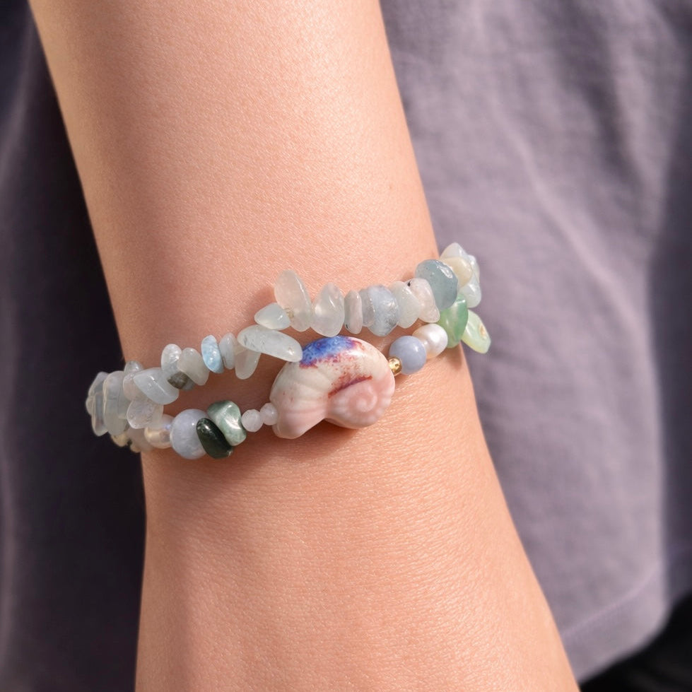 Beaded bracelet with a shell charm on a wrist against a neutral background