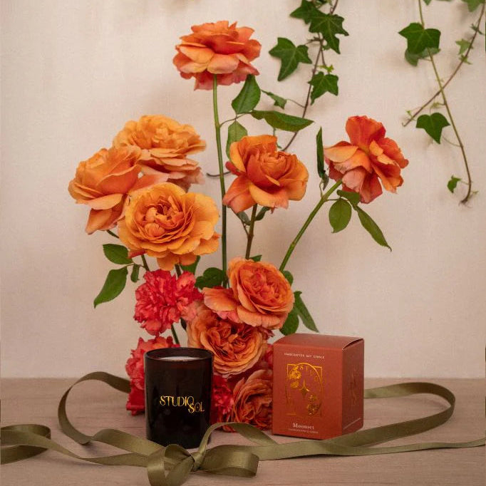 Bouquet of orange flowers with a candle and box on a wooden surface.