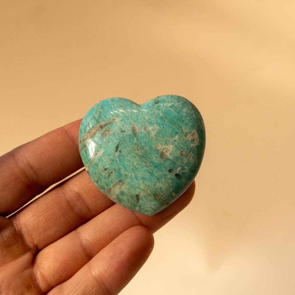 Heart-shaped Amazonite stone held in a hand against a beige background