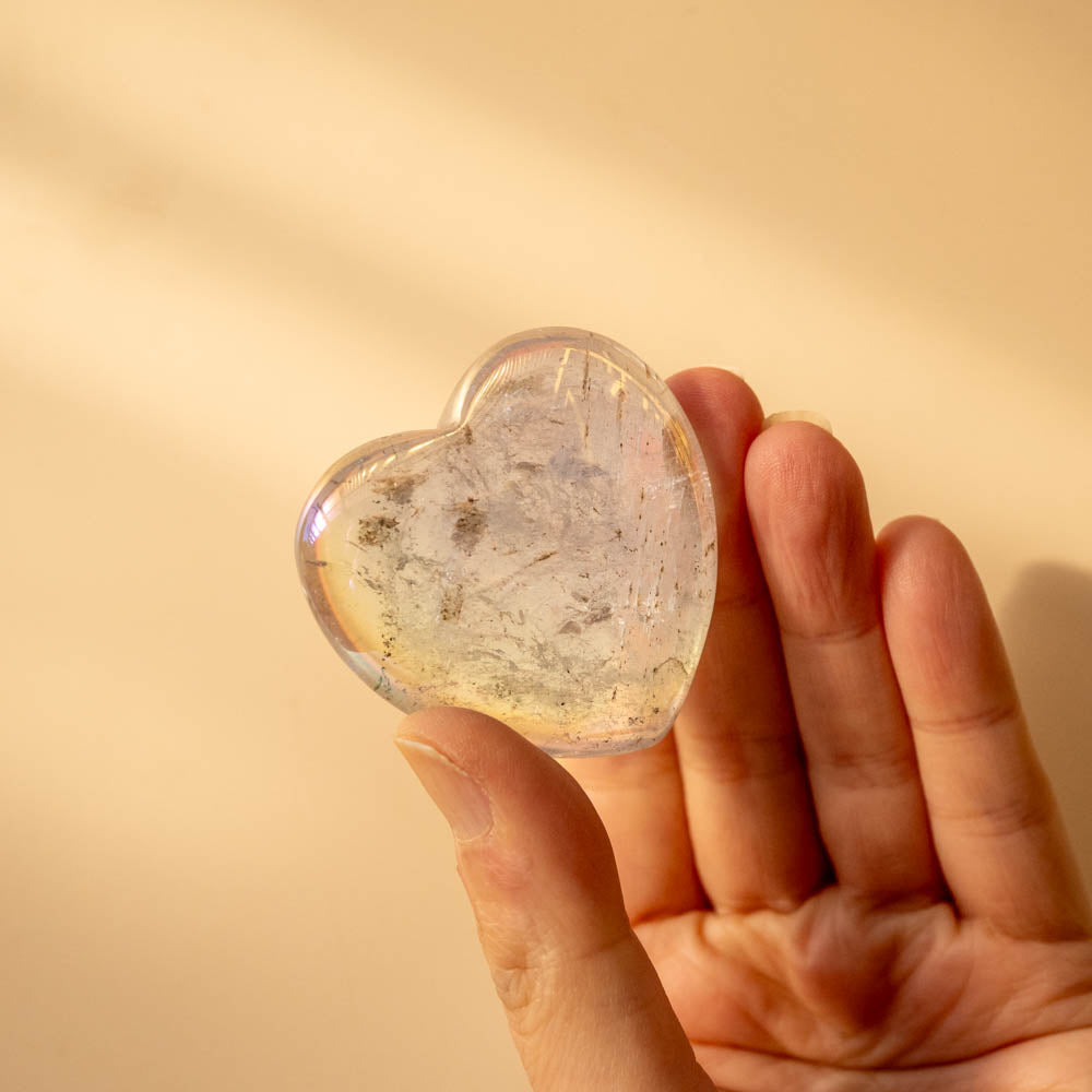 Heart-shaped Angel Aura crystal held in a hand against a warm beige background