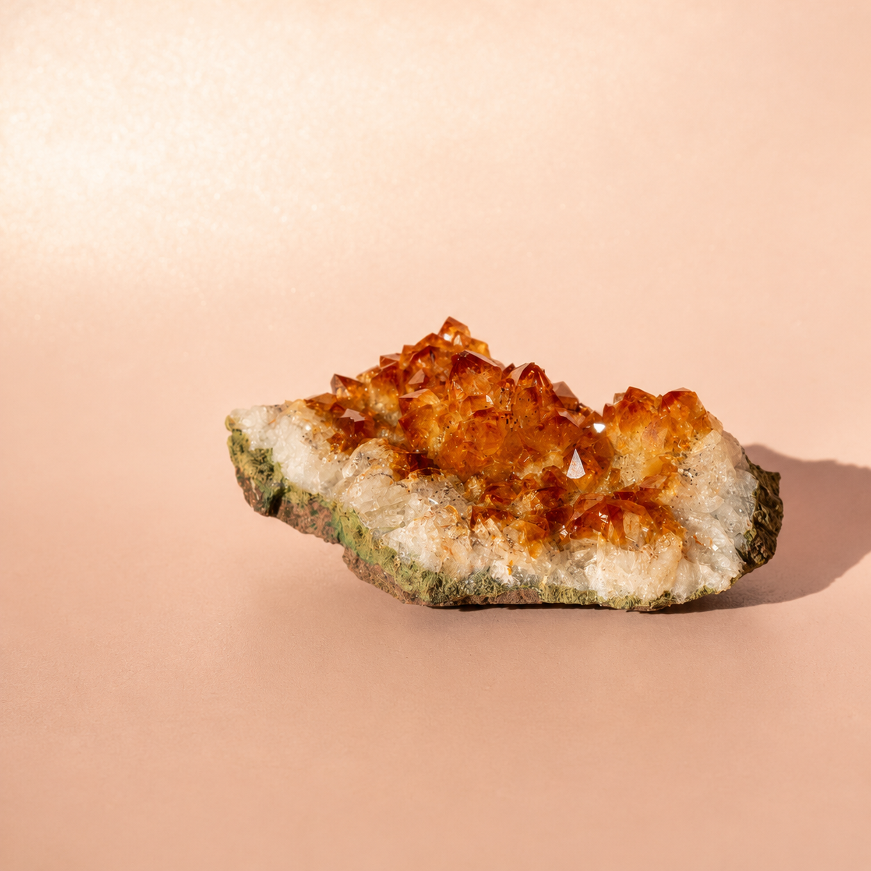 A natural citrine crystal cluster specimen with orange-brown translucent points on a pale matrix, photographed on a smooth warm peach background.