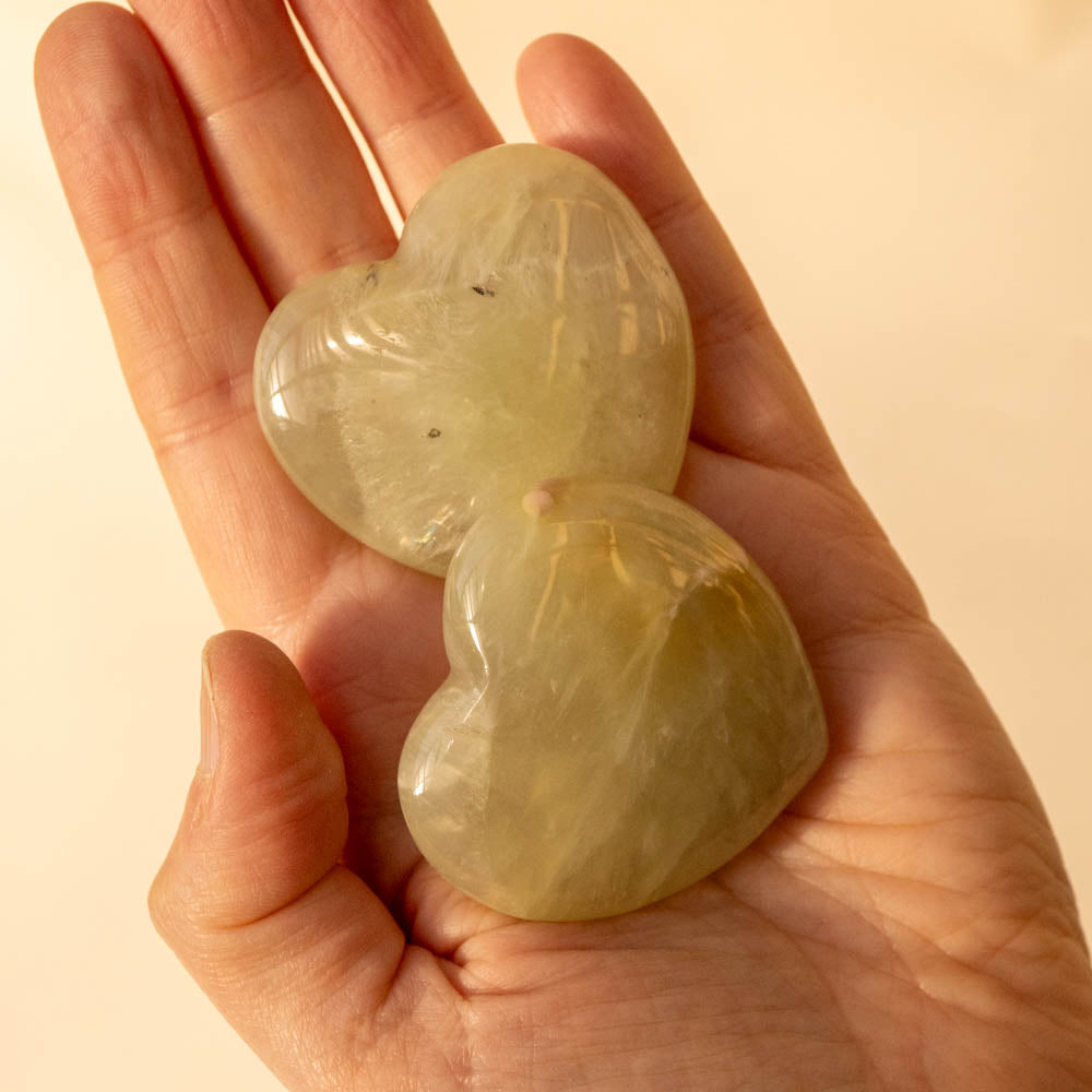 Heart-shaped Prehnite stones held in a hand against a beige background