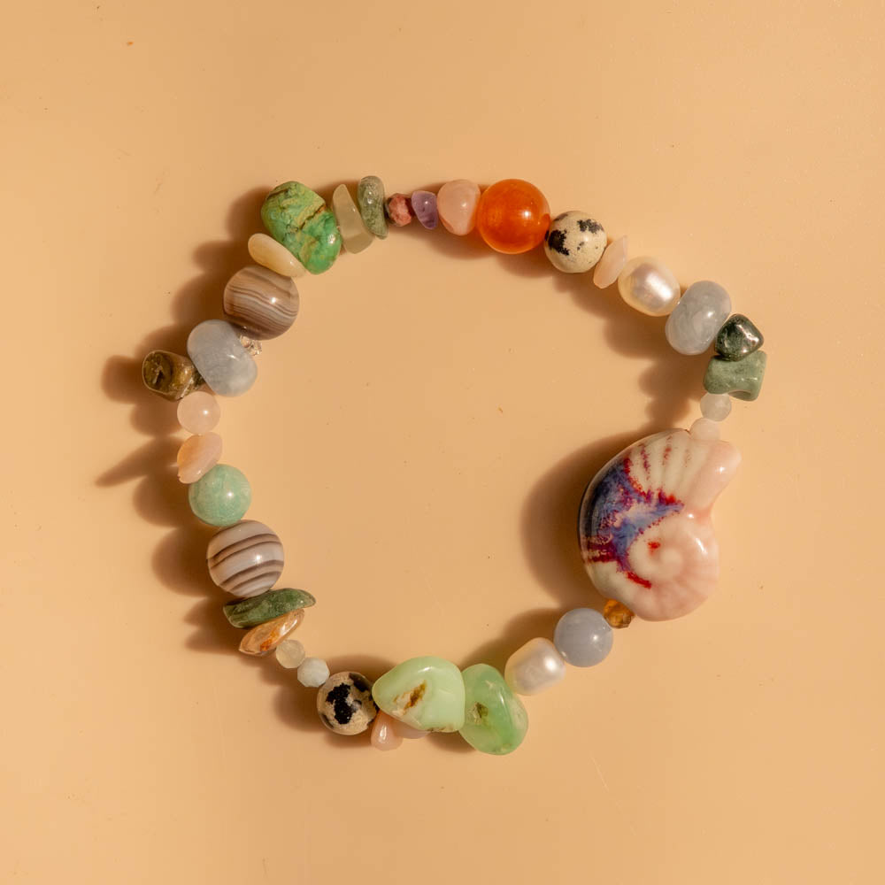 Multicolored beaded bracelet with a shell charm on a beige background