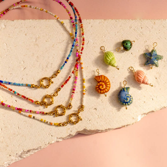 Colorful beaded necklace with various small decorative charms on a textured surface.