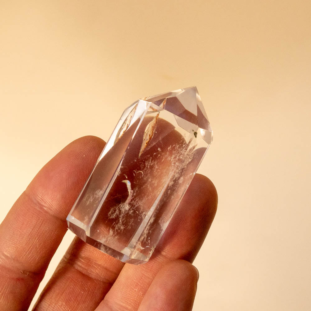 Clear quartz crystal held in a hand against a beige background