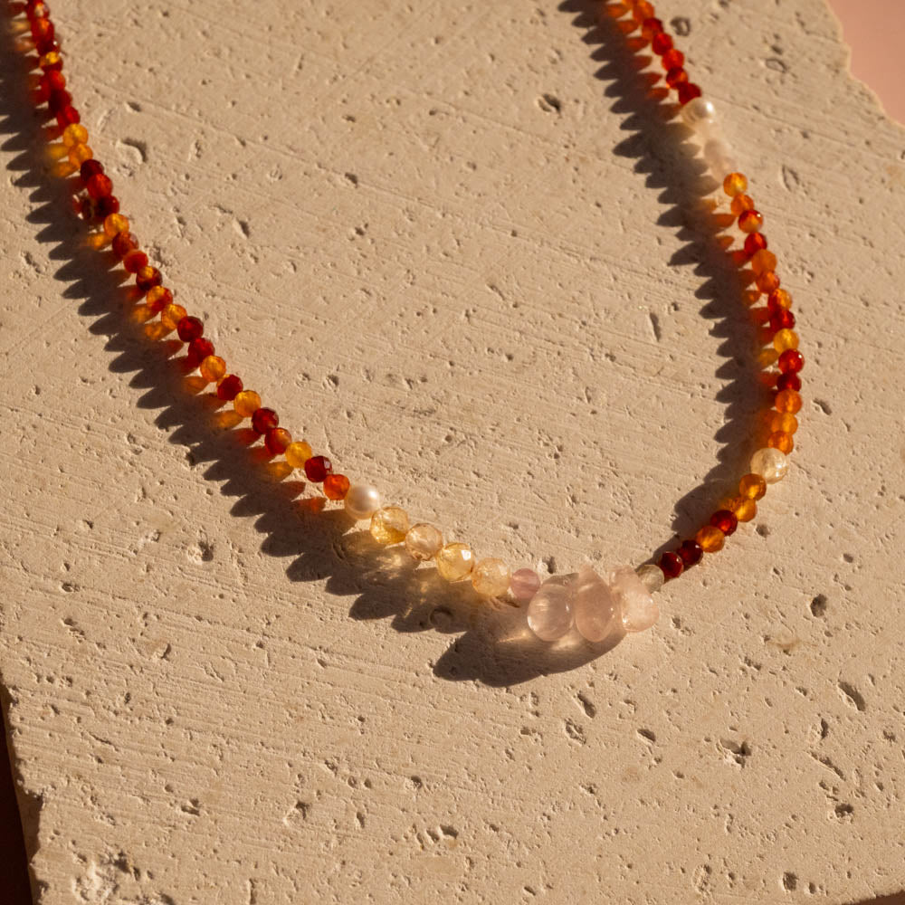 Necklace with red, orange, and pink beads on a textured beige surface