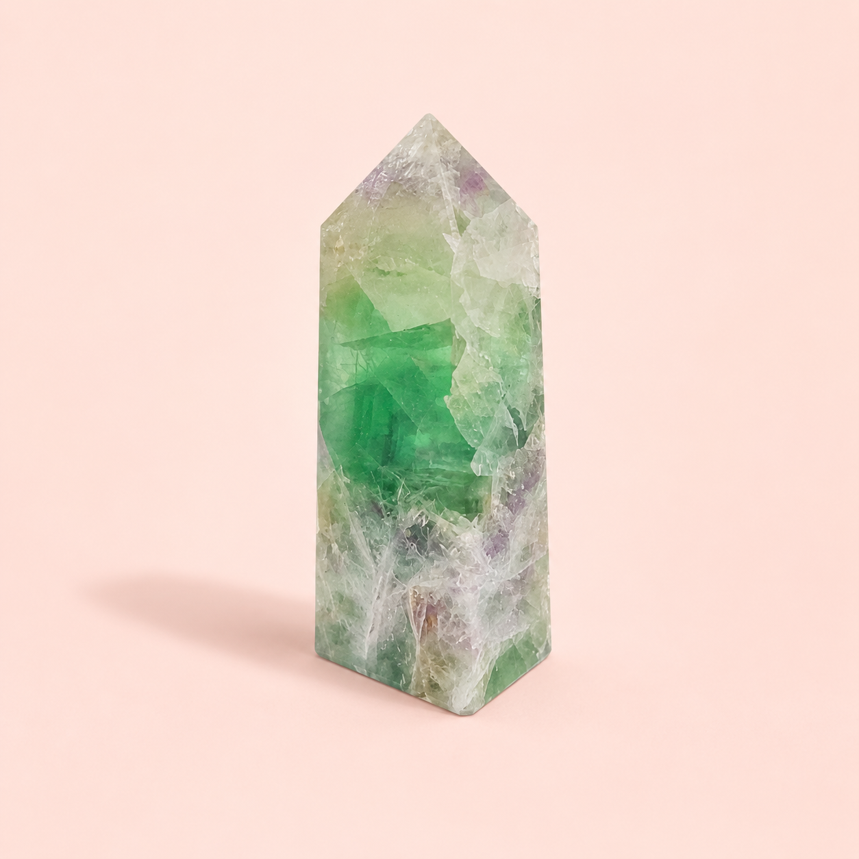 A polished fluorite crystal tower with natural green, purple, and white marbling, standing upright on a soft pink background.