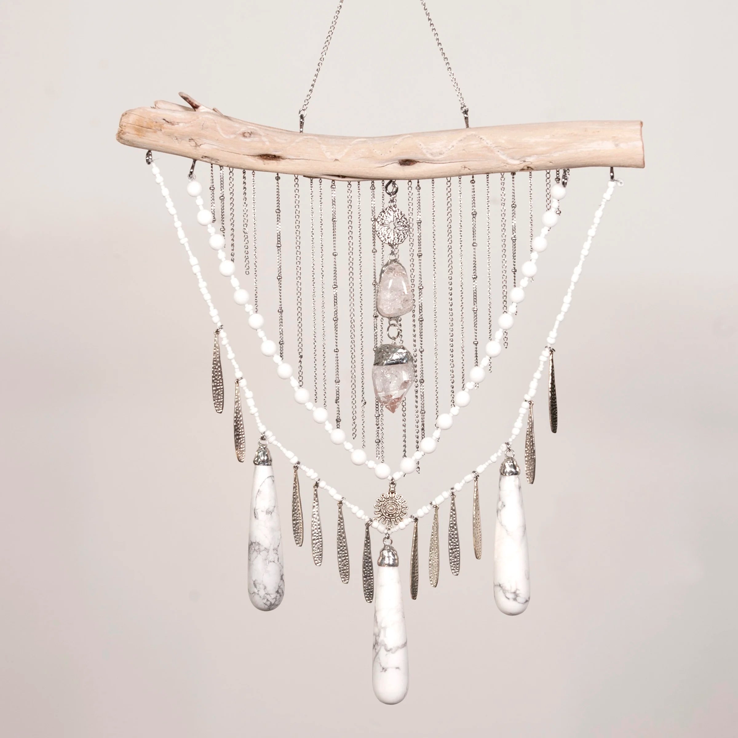 Decorative hanging Howlite with Quartz crystals and feathers on a neutral background