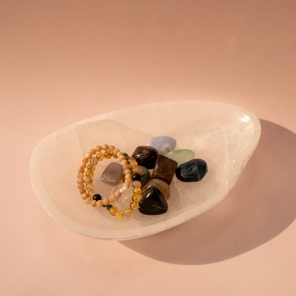 Set of beaded bracelets on a selenite crystal dish against a pink background