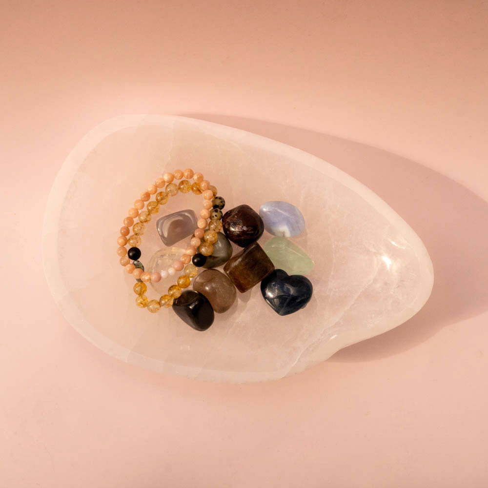 Set of beaded bracelets and stones on a Selenite Crystal bowl against a pink background