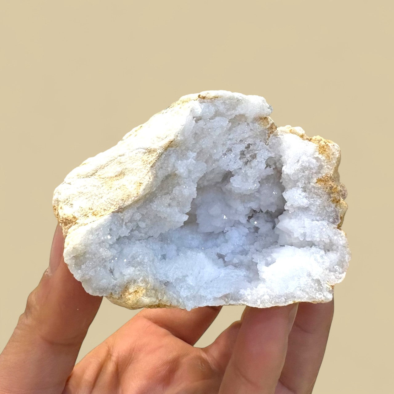 Hand holding a crystal geode rock against a beige background