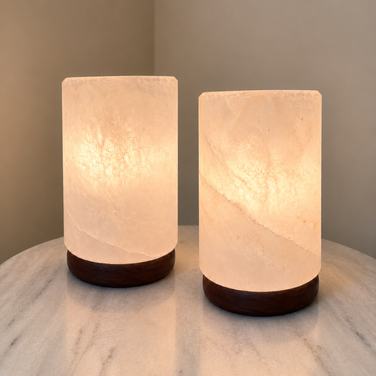 Two white cylinder salt lamps sided by side on a marble side table