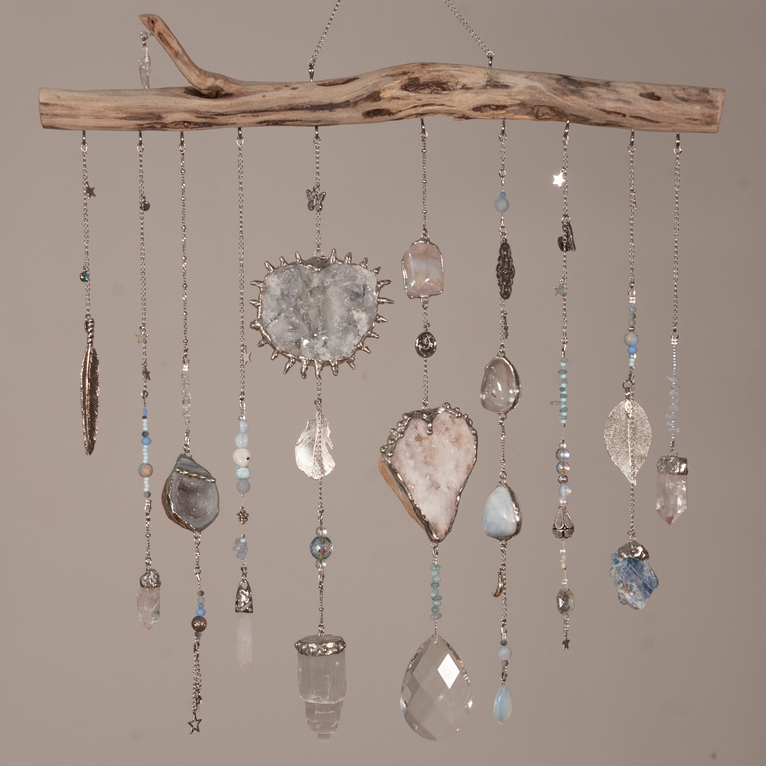 Decorative hanging mobile with crystals and a branch on a plain background