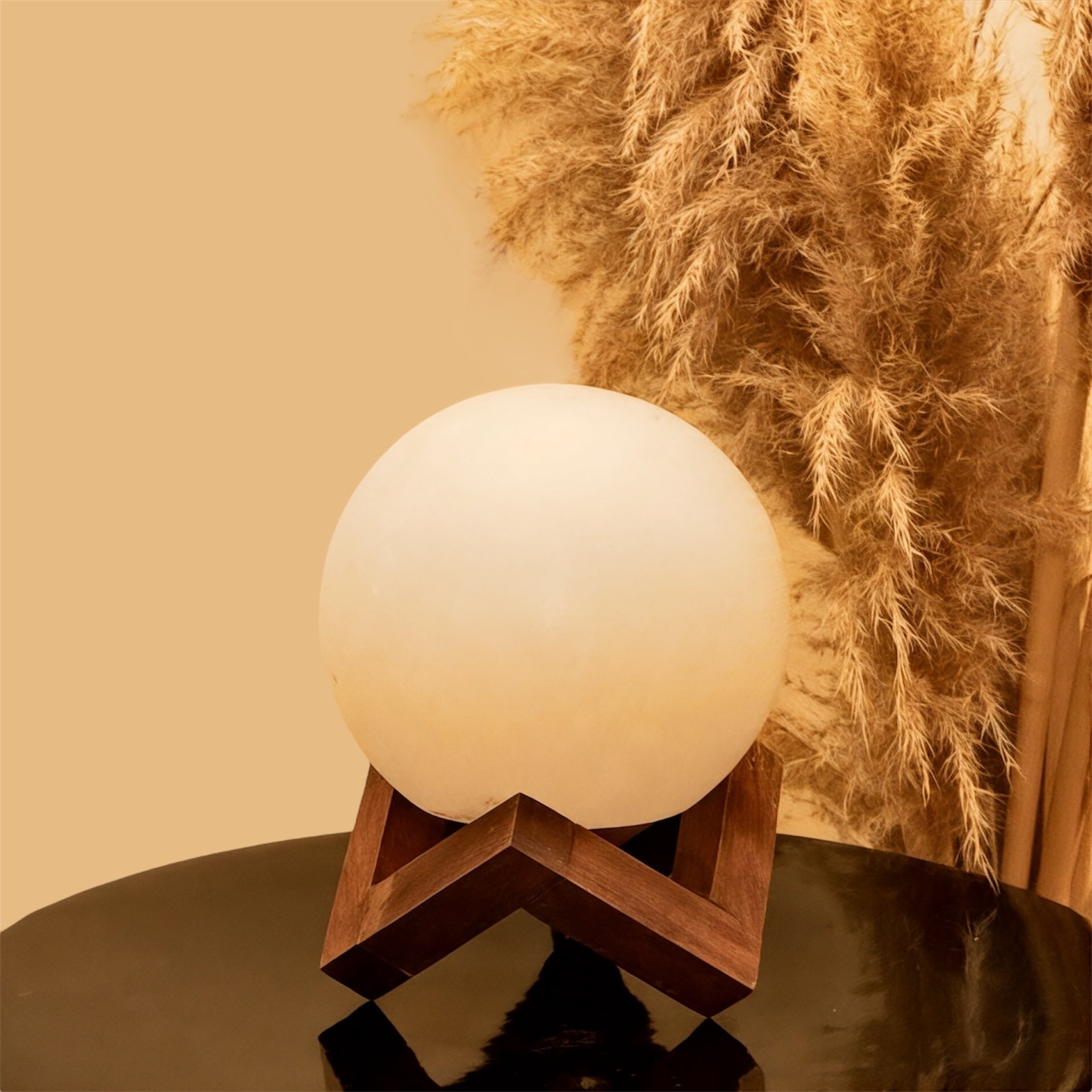 White salt spherical lamp on a wooden stand against a beige background with pampas grass.