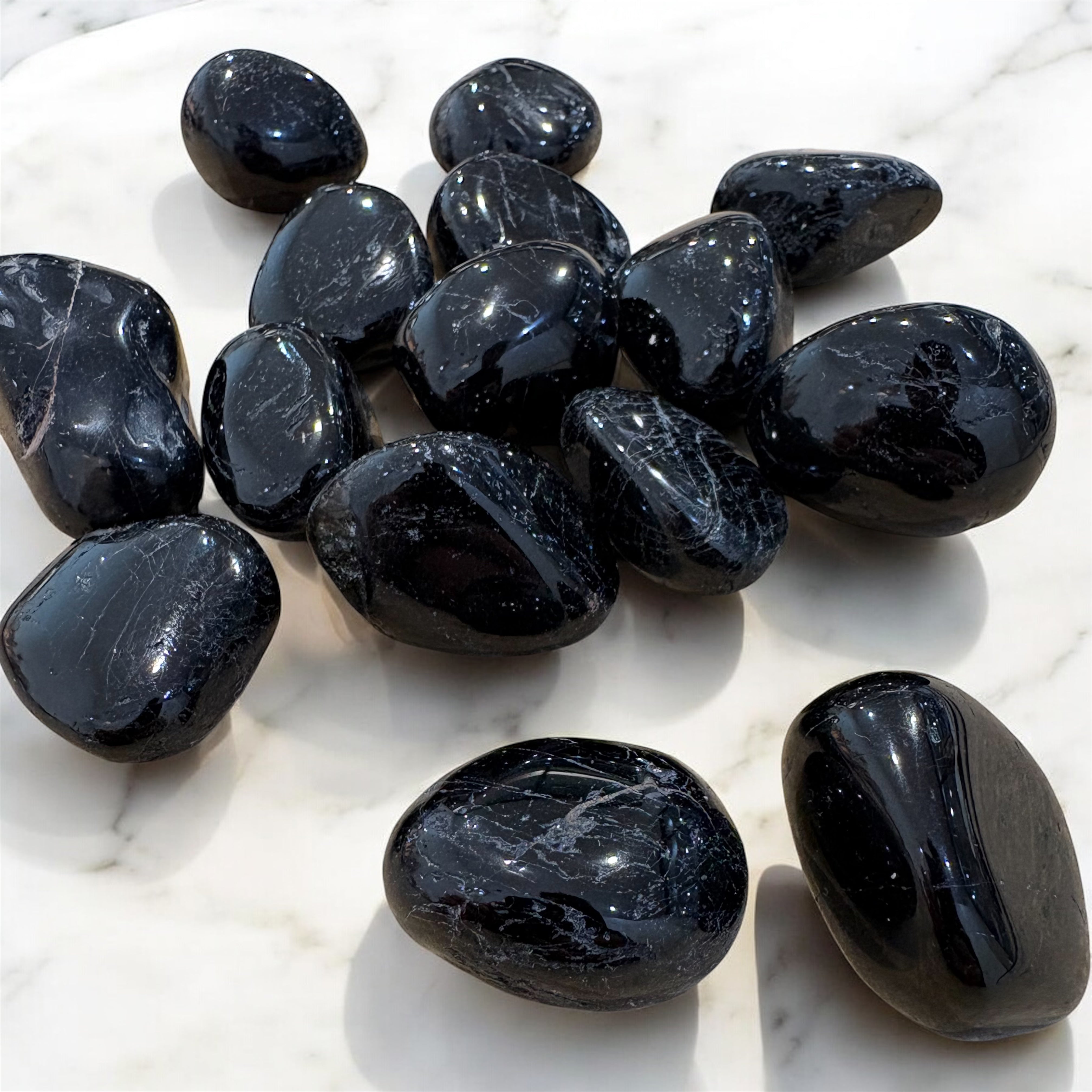Black Tourmaline Tumbled Stones on a white marble surface