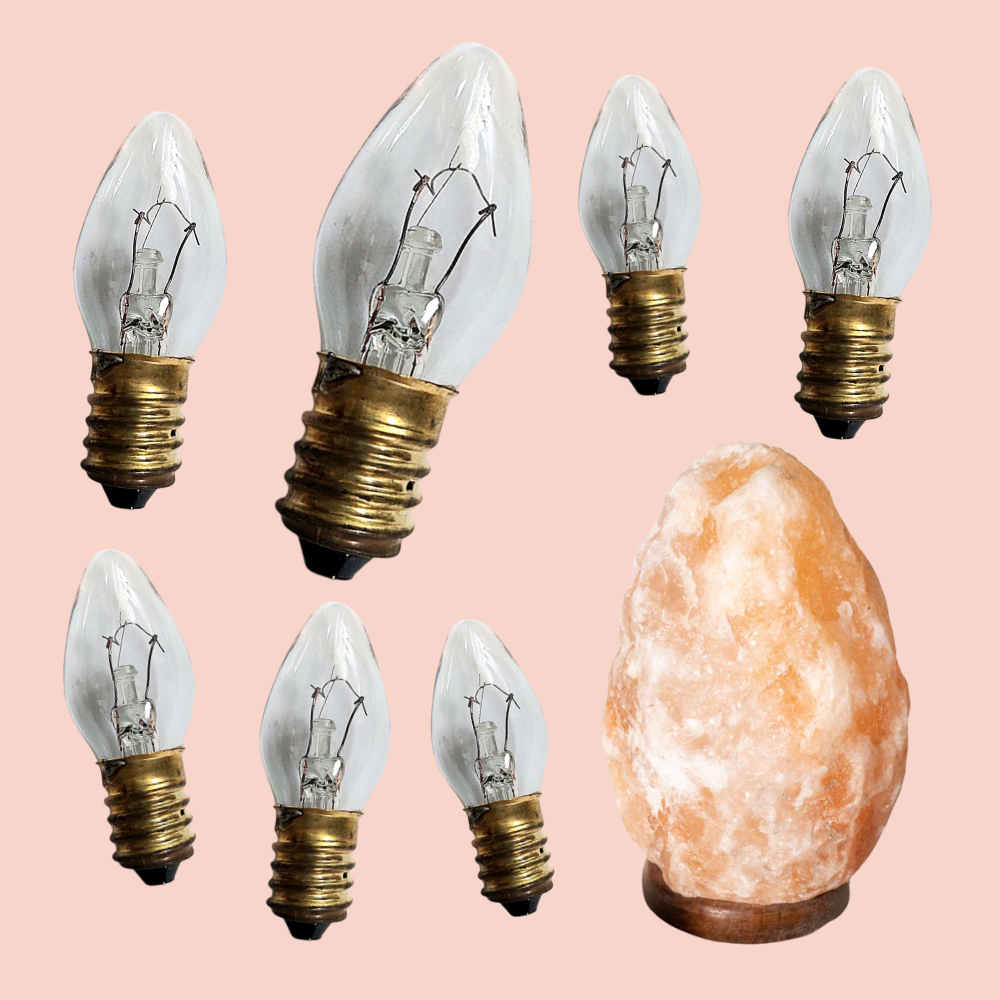 Set of six clear light bulbs with gold bases and a Himalayan salt lamp on a pink background