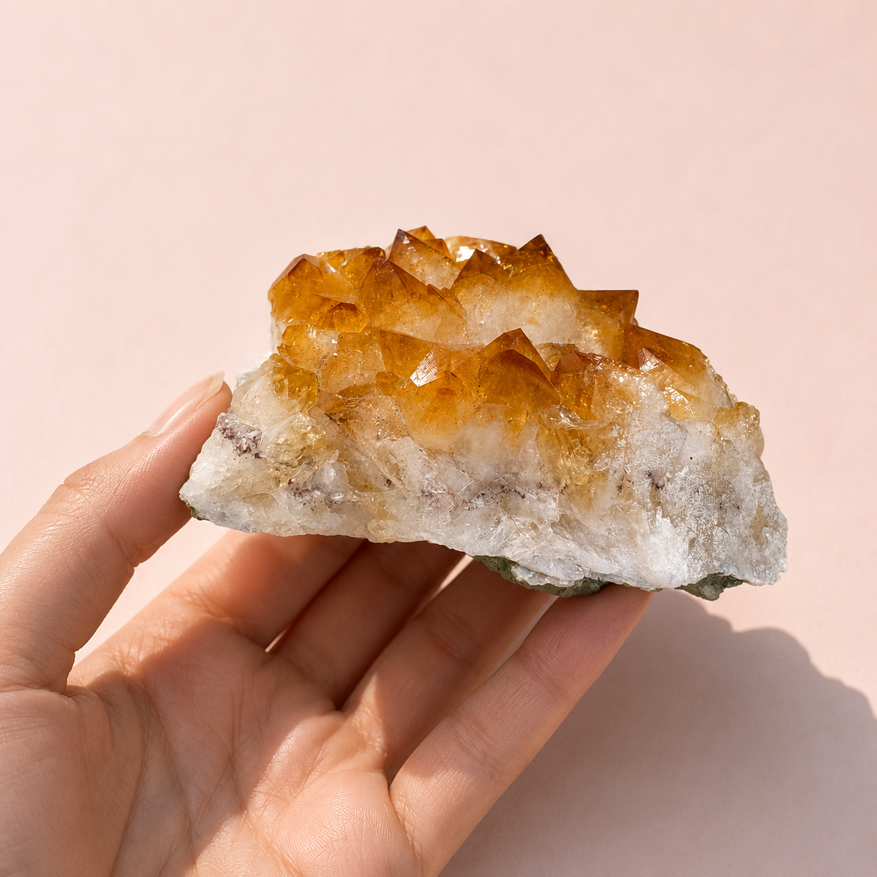Hand holding a Citrine Crystal Cluster with a pink background