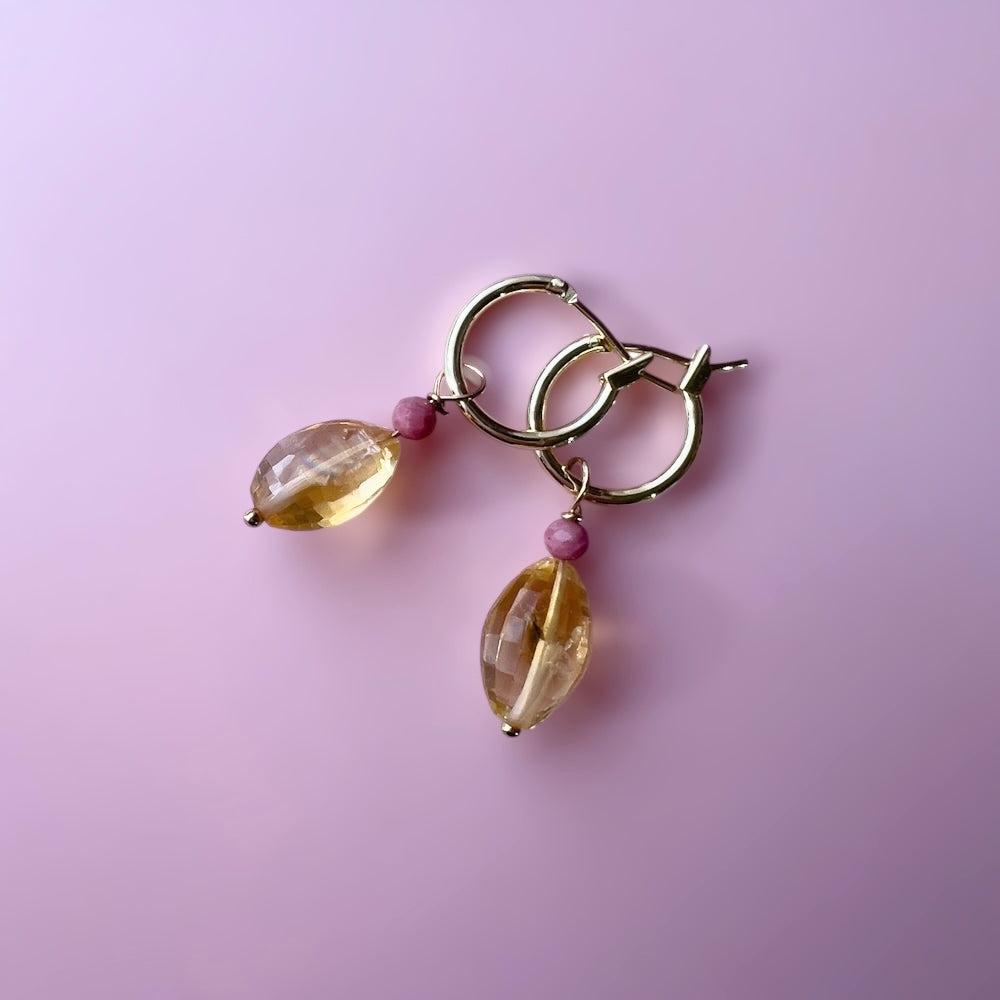 Gold hoop earring with citrine and rhodonite gemstones and pink beads on a pink background