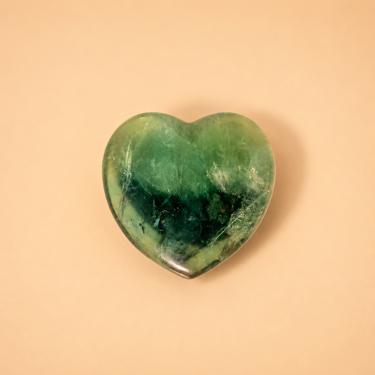 Heart-shaped green fluorite crystal on a beige background