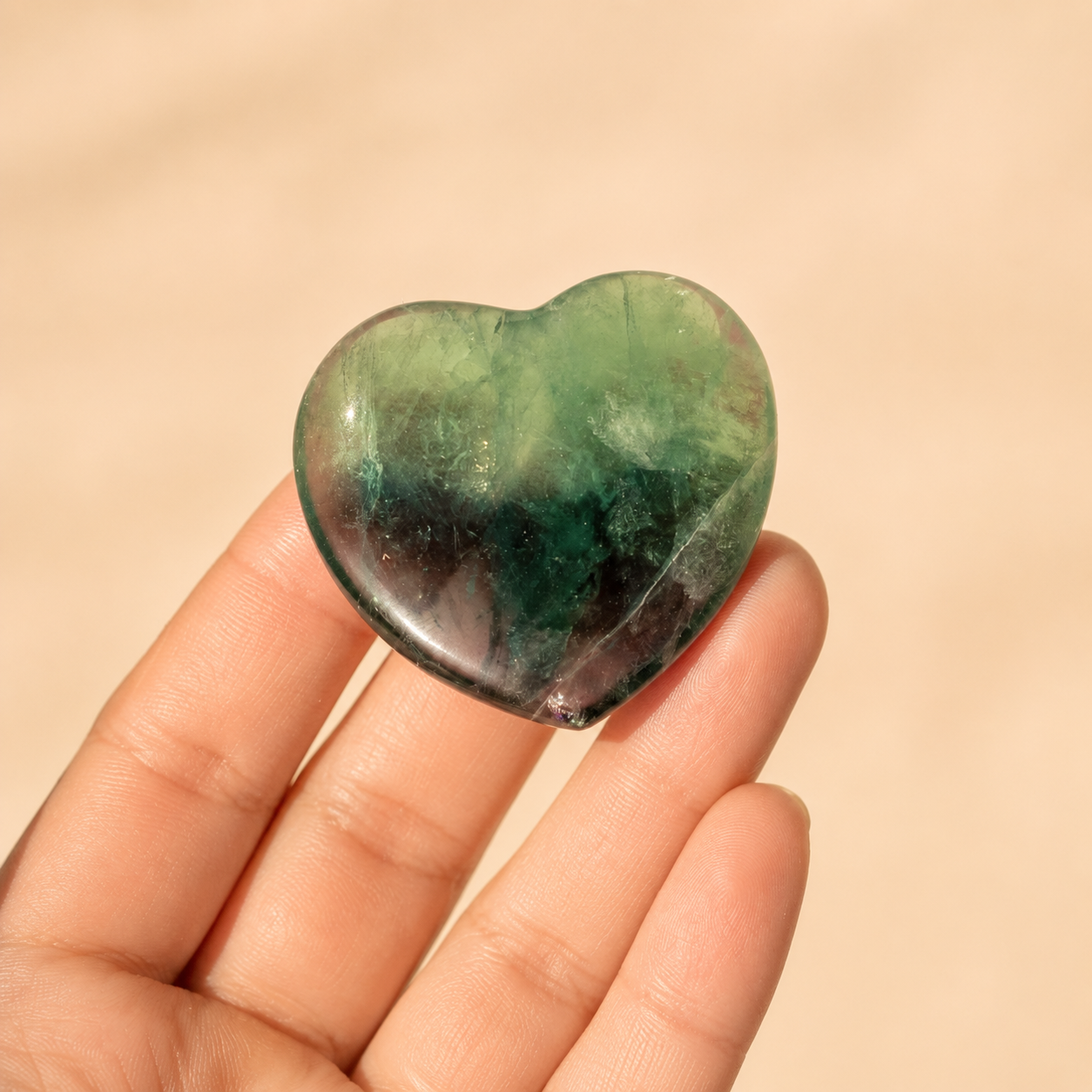 Heart-shaped green fluorite crystal held in a hand against a beige background