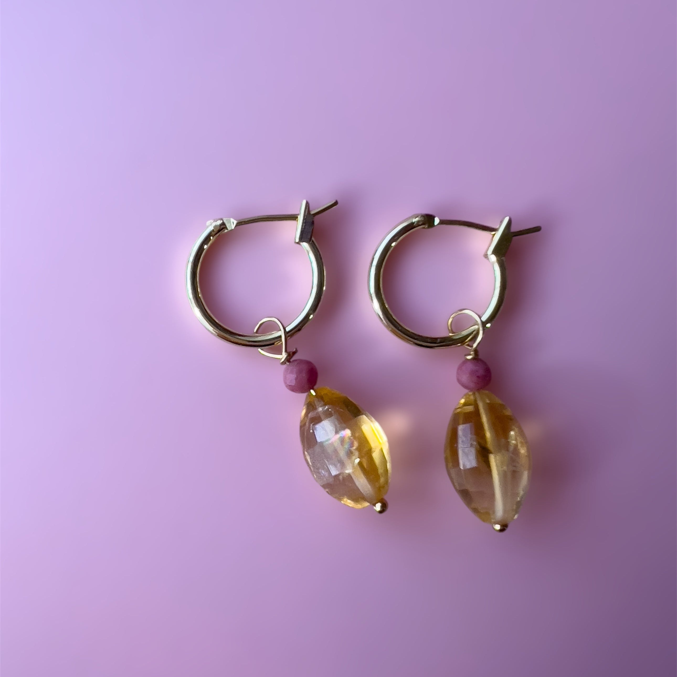 Gold hoop earrings with citrine and rhodonite beads on a pink background