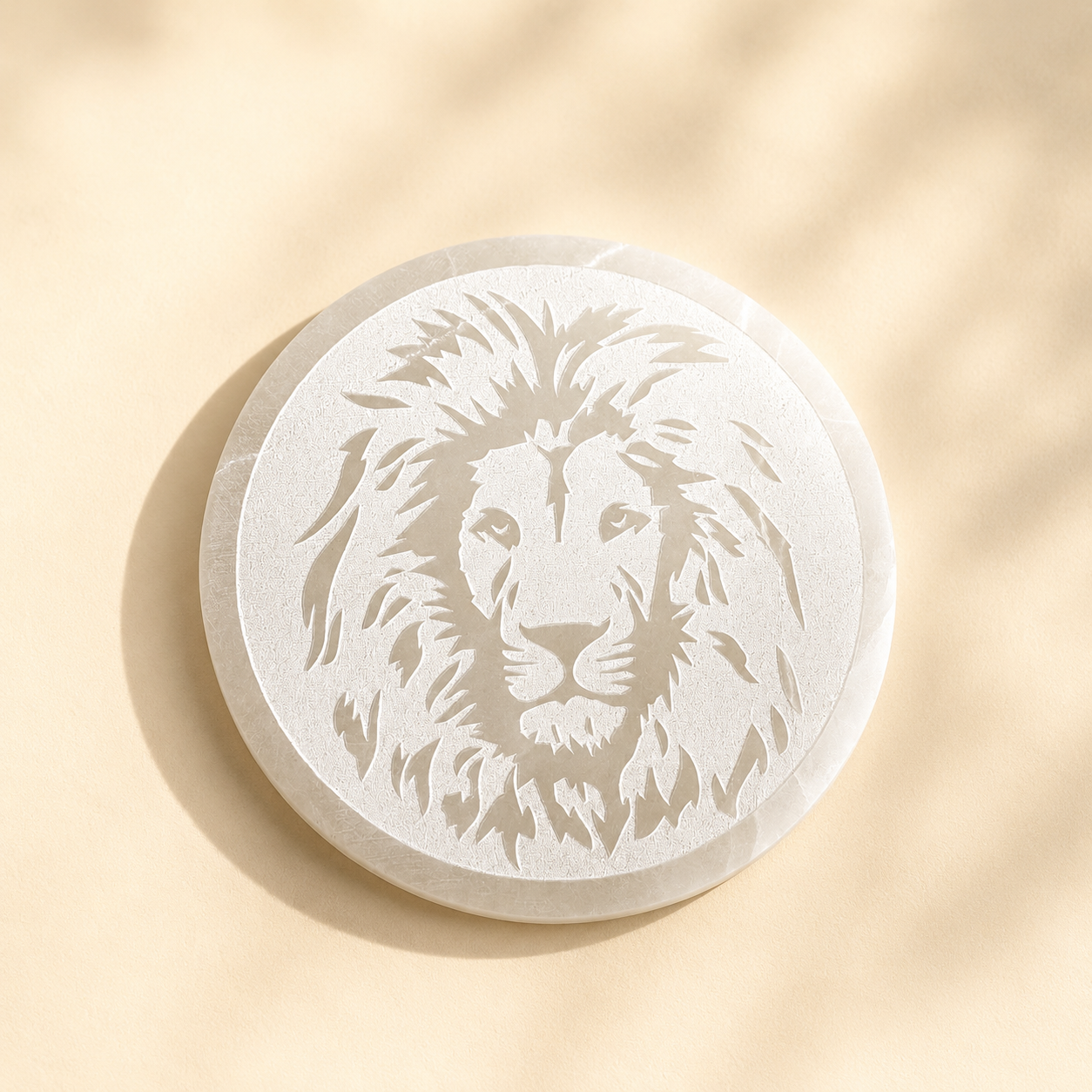 Round selenite crystal charging plate with a lion engraving on a beige background