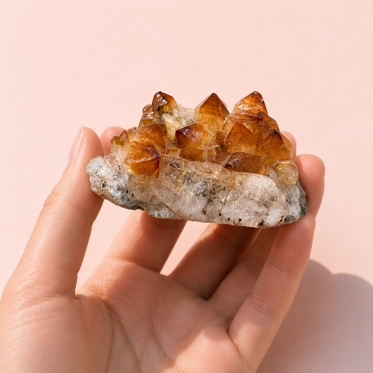 Hand holding a citrine cluster against a pink background