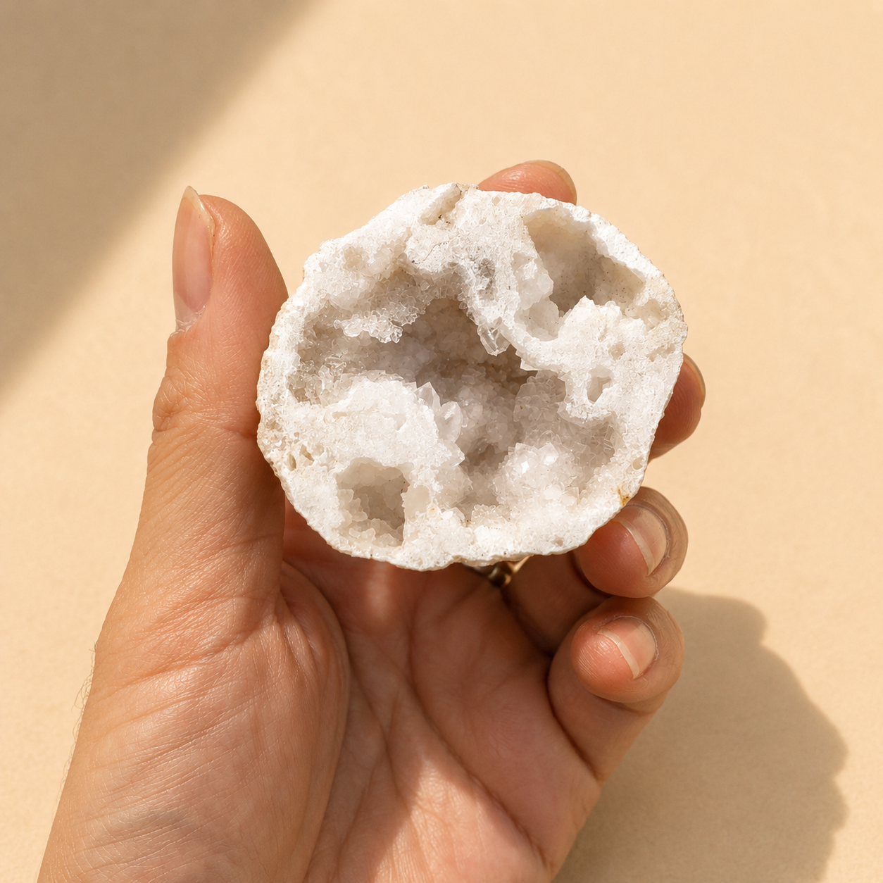Hand holding a white crystal rock against a beige background