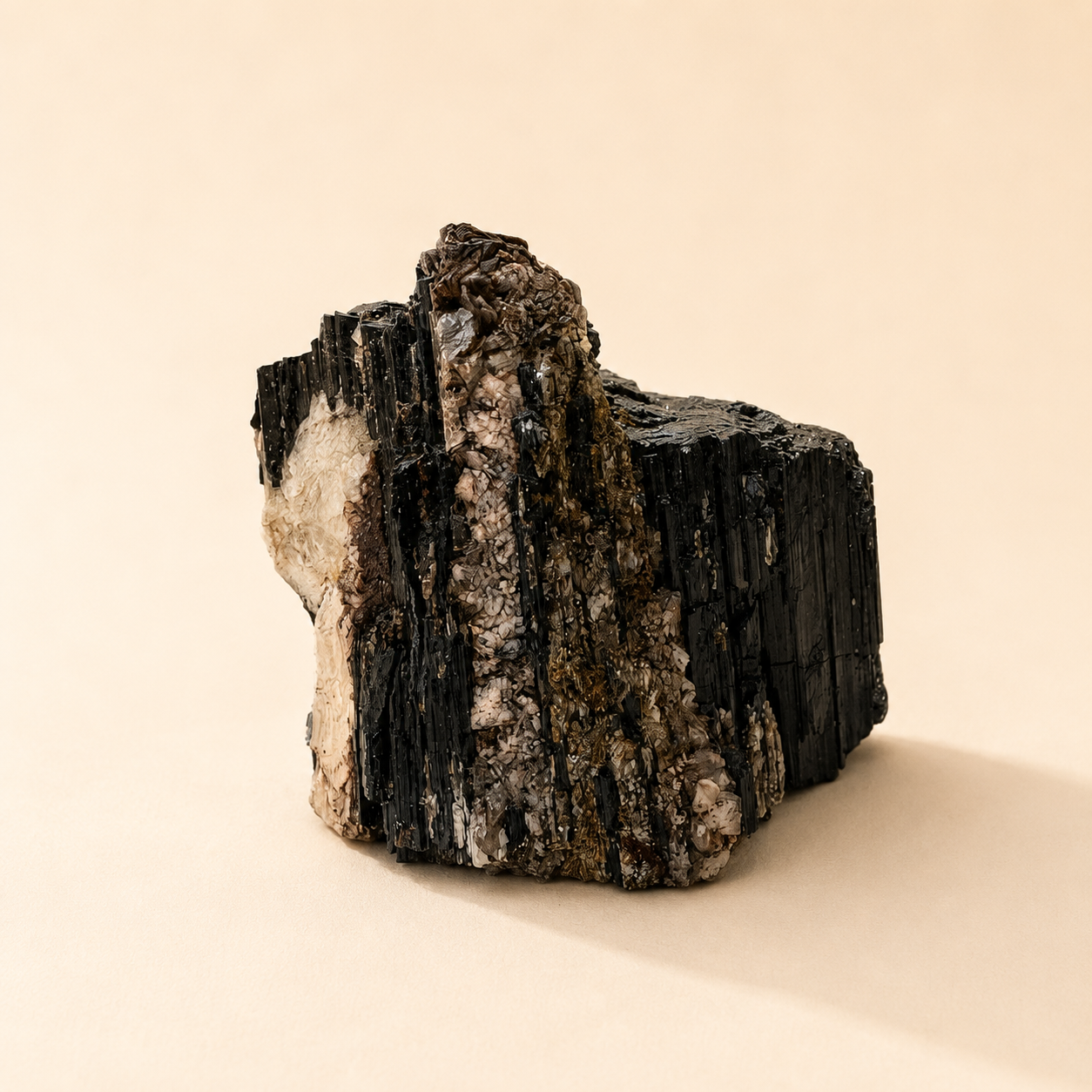A raw black tourmaline with mica, photographed on a clean beige background.