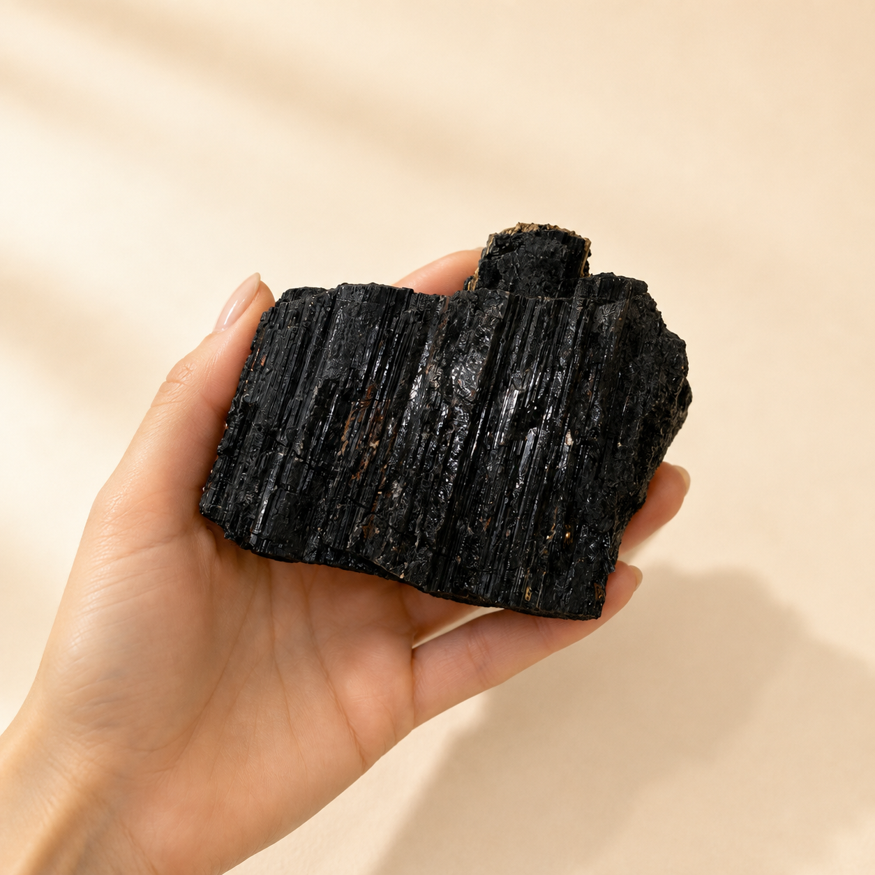 A hand holding black tourmaline against a soft beige background.