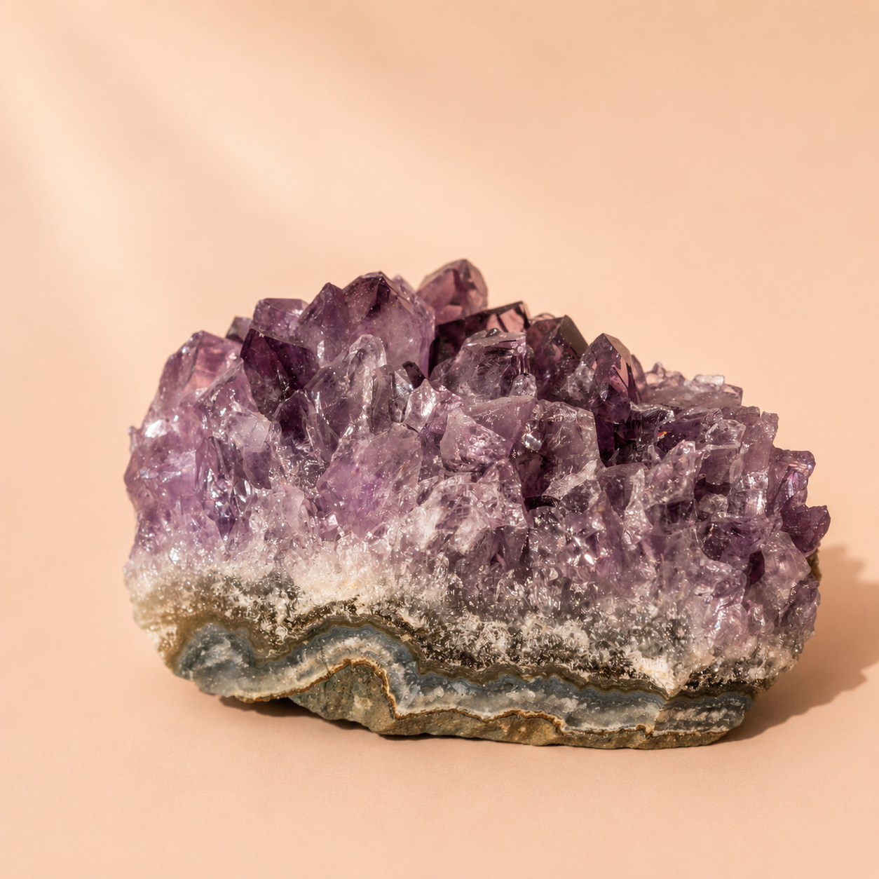A natural amethyst crystal cluster with a wavy band of blue-gray and green matrix, displayed on a warm beige background.