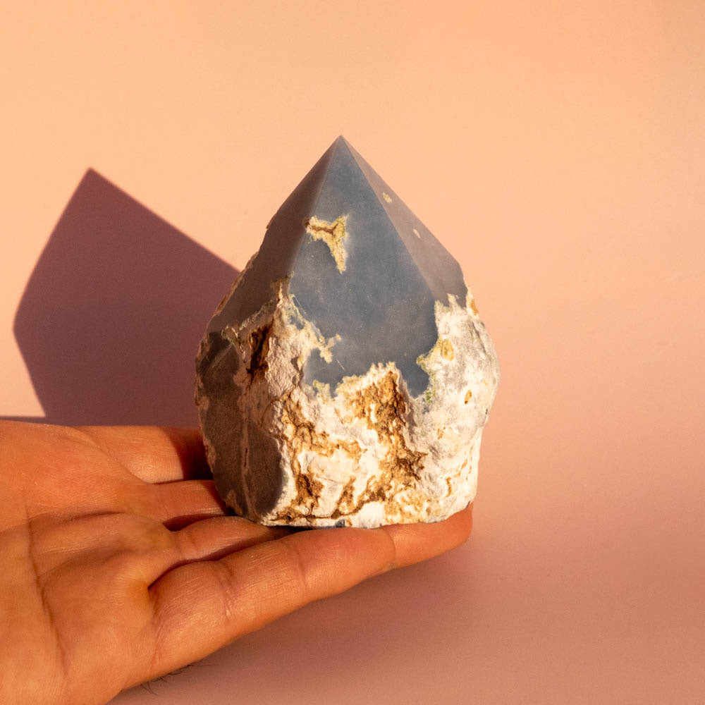 Hand holding a large angelite crystal against a pink background