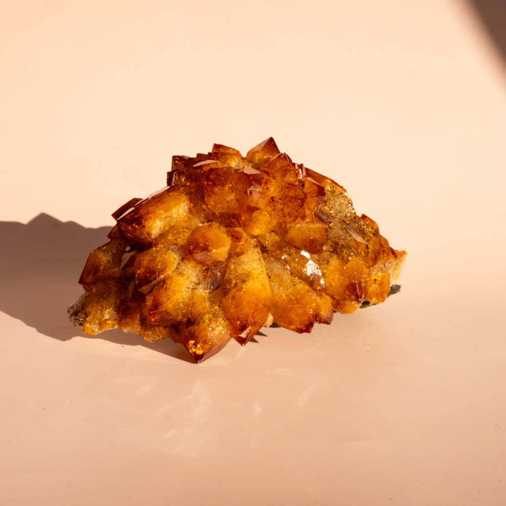 A cluster citrine, photographed on a smooth warm beige surface with a soft shadow to the left.