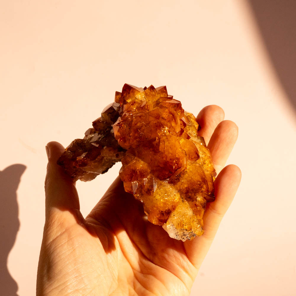 A hand citrine crystal cluster against a warm beige background.