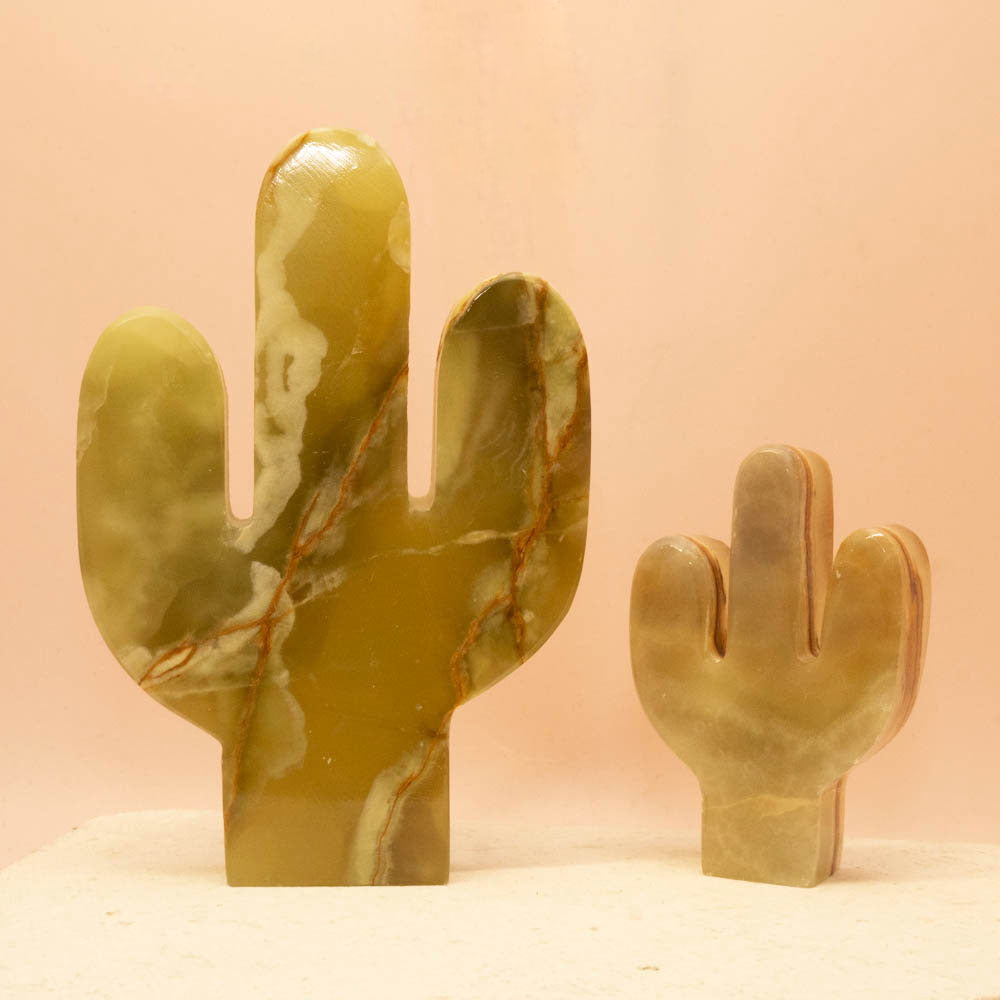 Two Green Onyx cactus sculptures on a beige surface with a pink background
