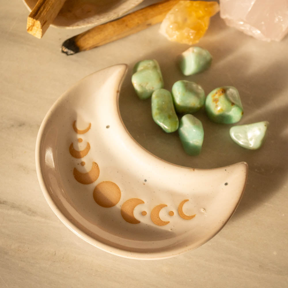 Ceramic dish with moon design containing green stones on a wooden surface.