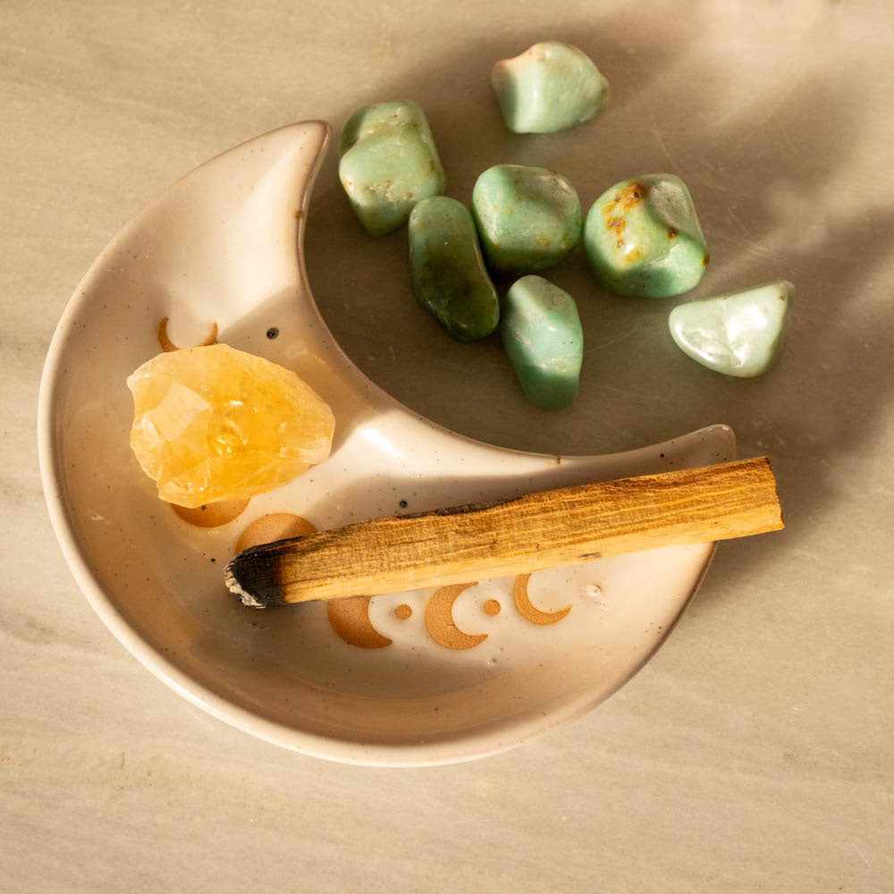 Moon crescent dish with turquoise stones, a citrine crystal, and palo santo on a marble table
