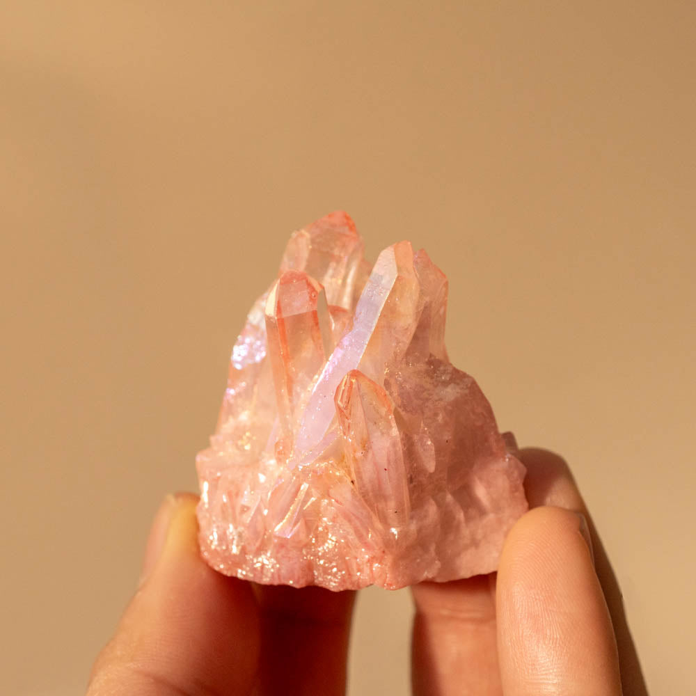 Hand holding a pink aura crystal against a beige background