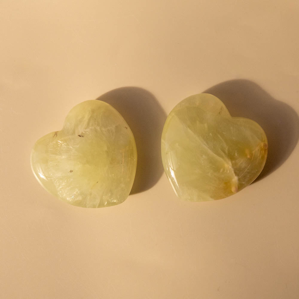 Two heart-shaped Prehnite stones on a beige background