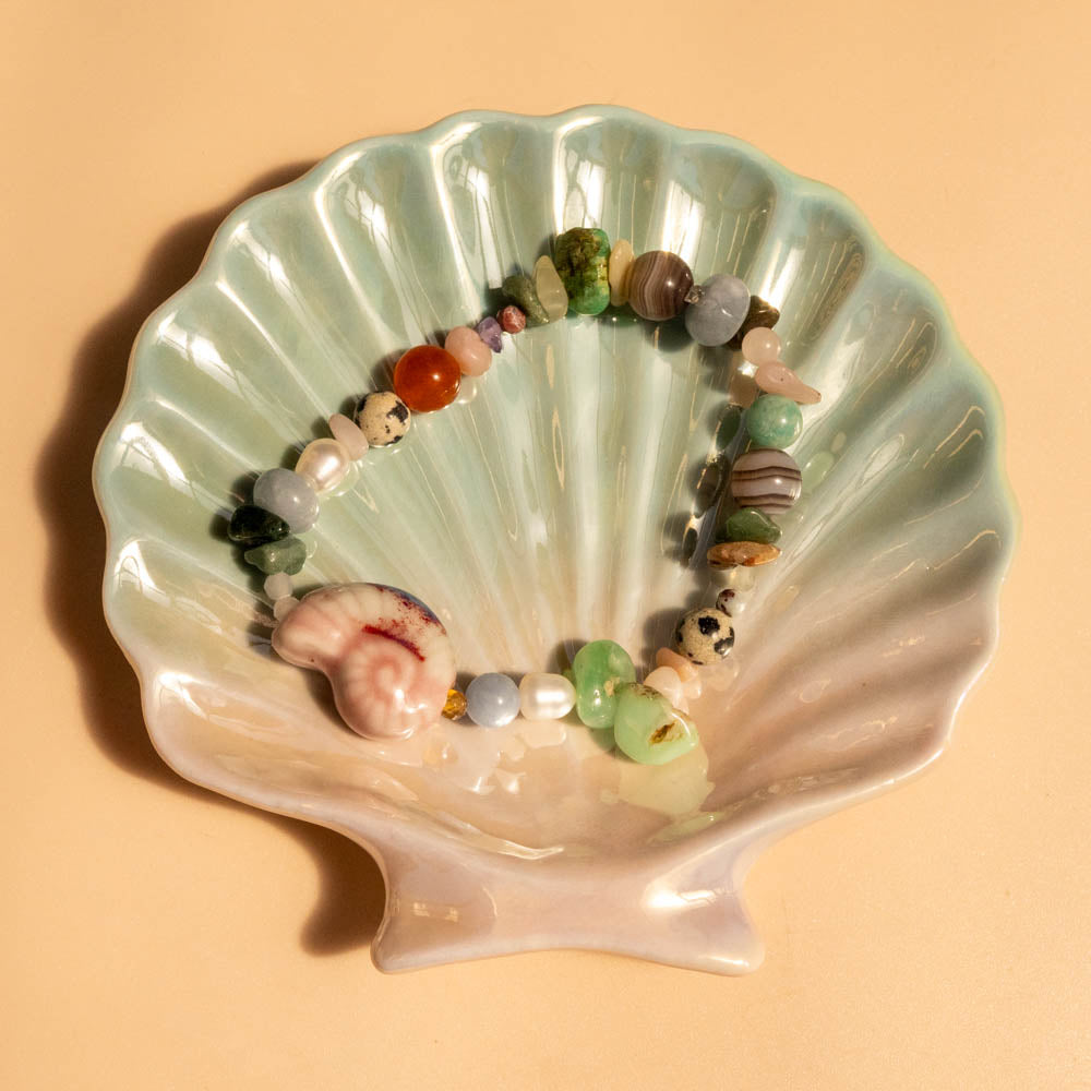 Shell-shaped dish with colorful beads and a pearl on a beige background