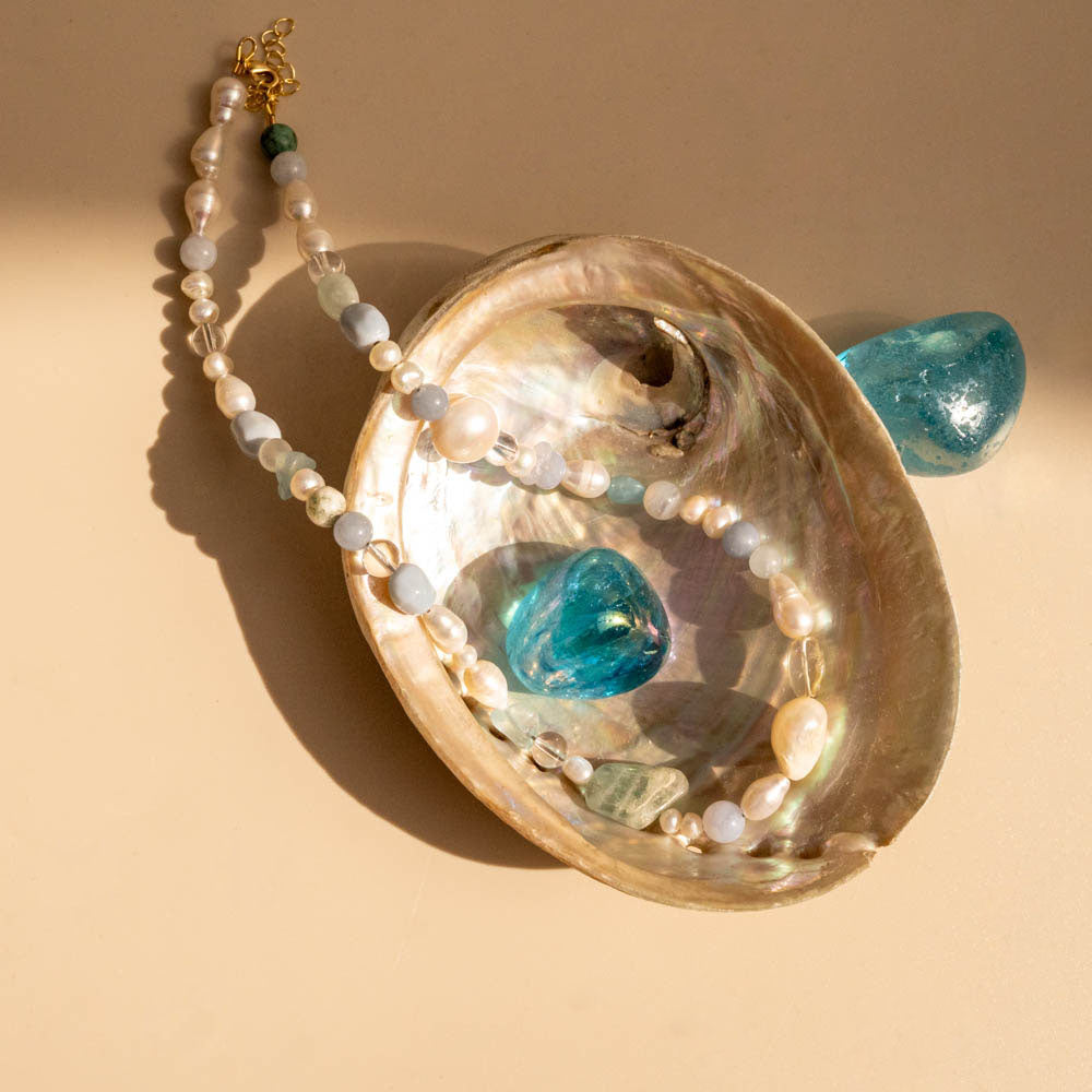 Necklace with pearls and blue stones in a shell on a beige background