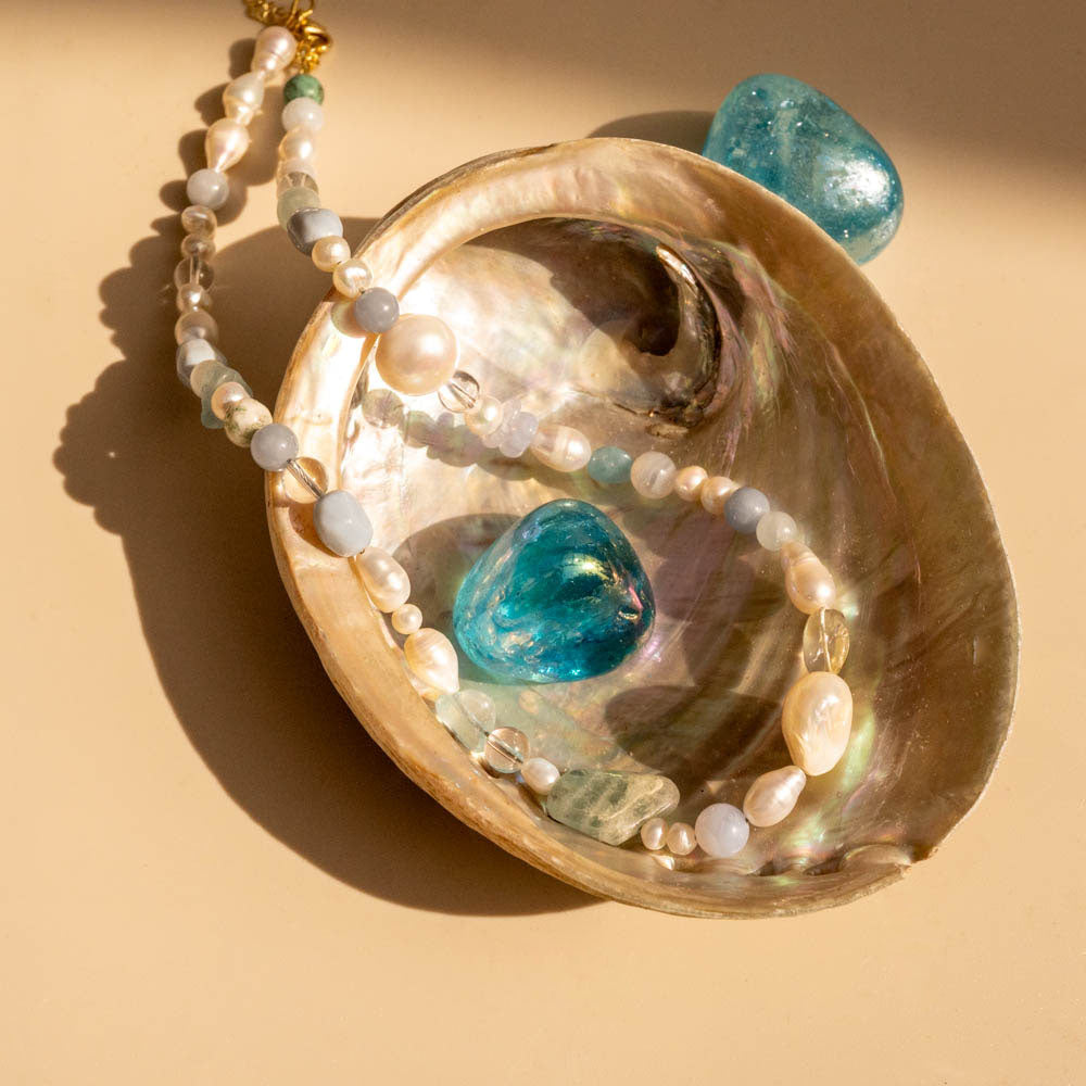 Necklace with pearls and blue stones in a shell on a beige background