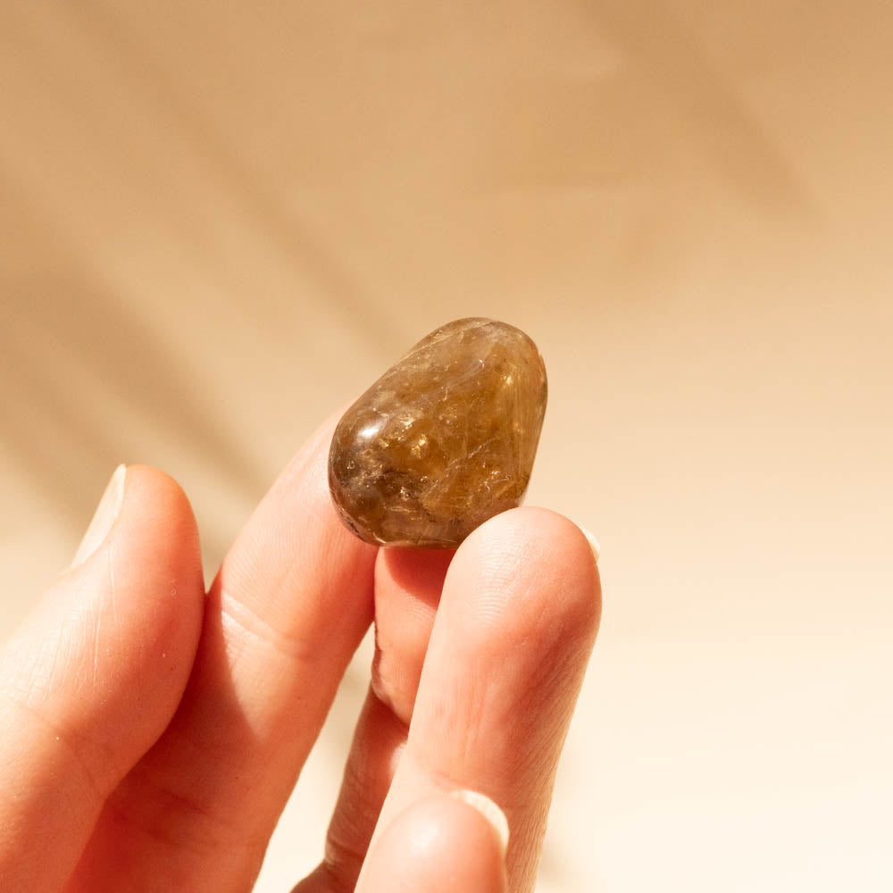 Hand holding a small Kundalini Citrine Tumbled Stones against a beige background