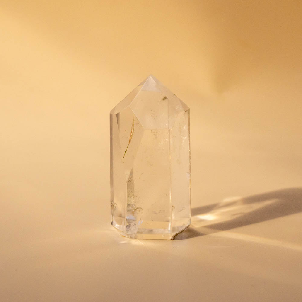 Clear quartz crystal point generator on a beige background