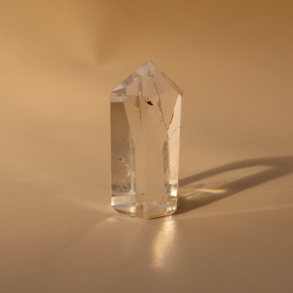 Clear quartz crystal point generator on a beige background