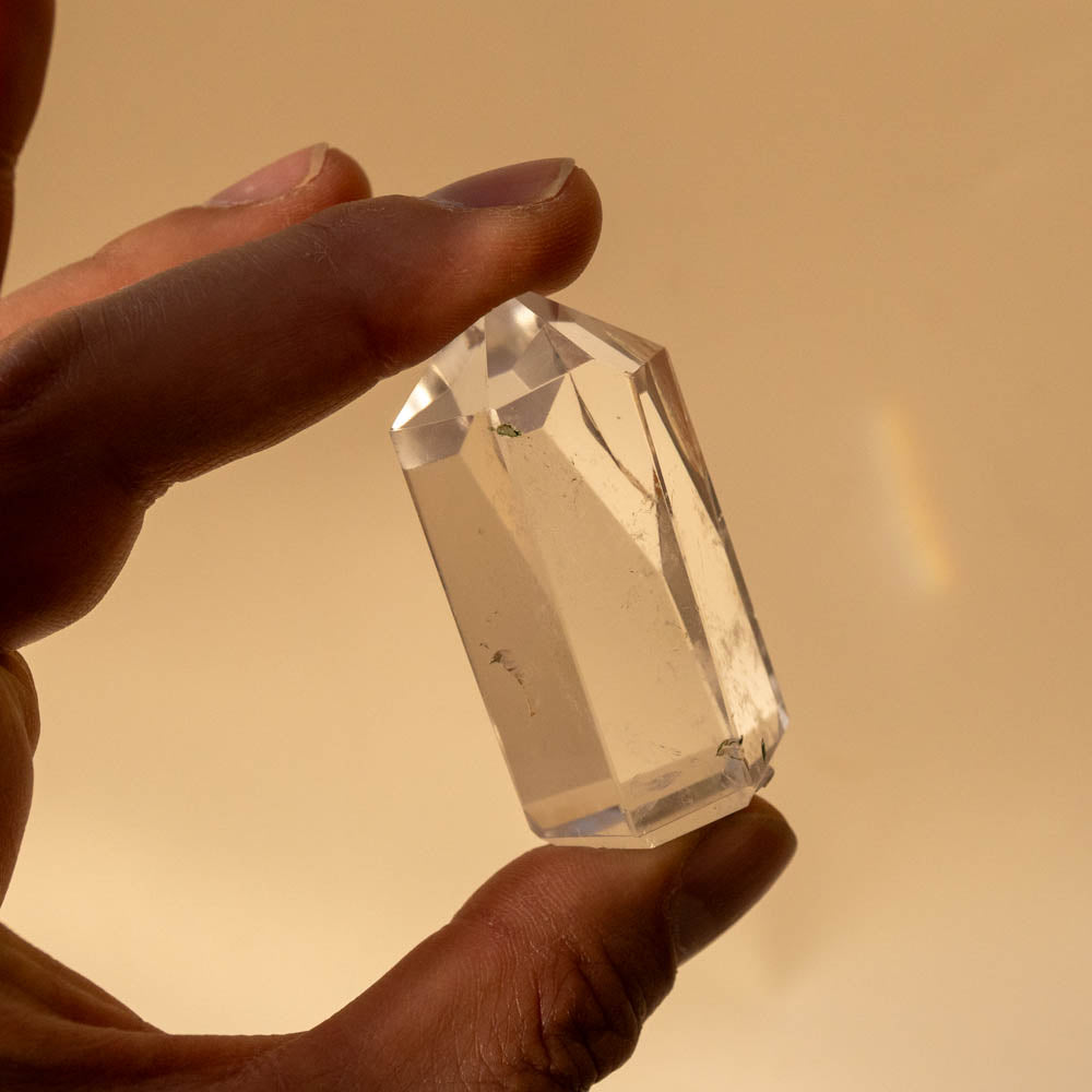 Hand holding a clear quartz crystal against a warm beige background