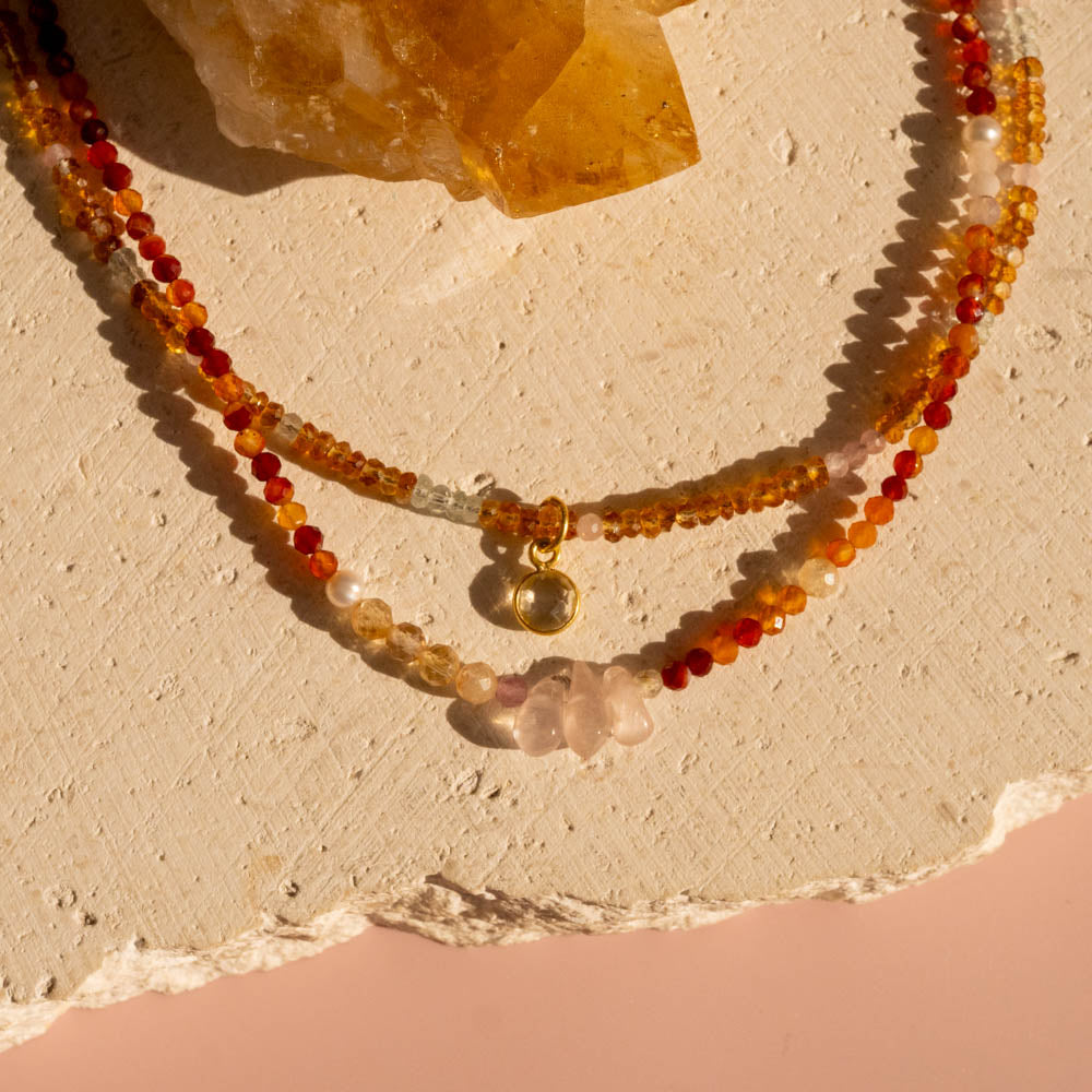 Beaded necklaces with orange and red stones on a textured beige surface