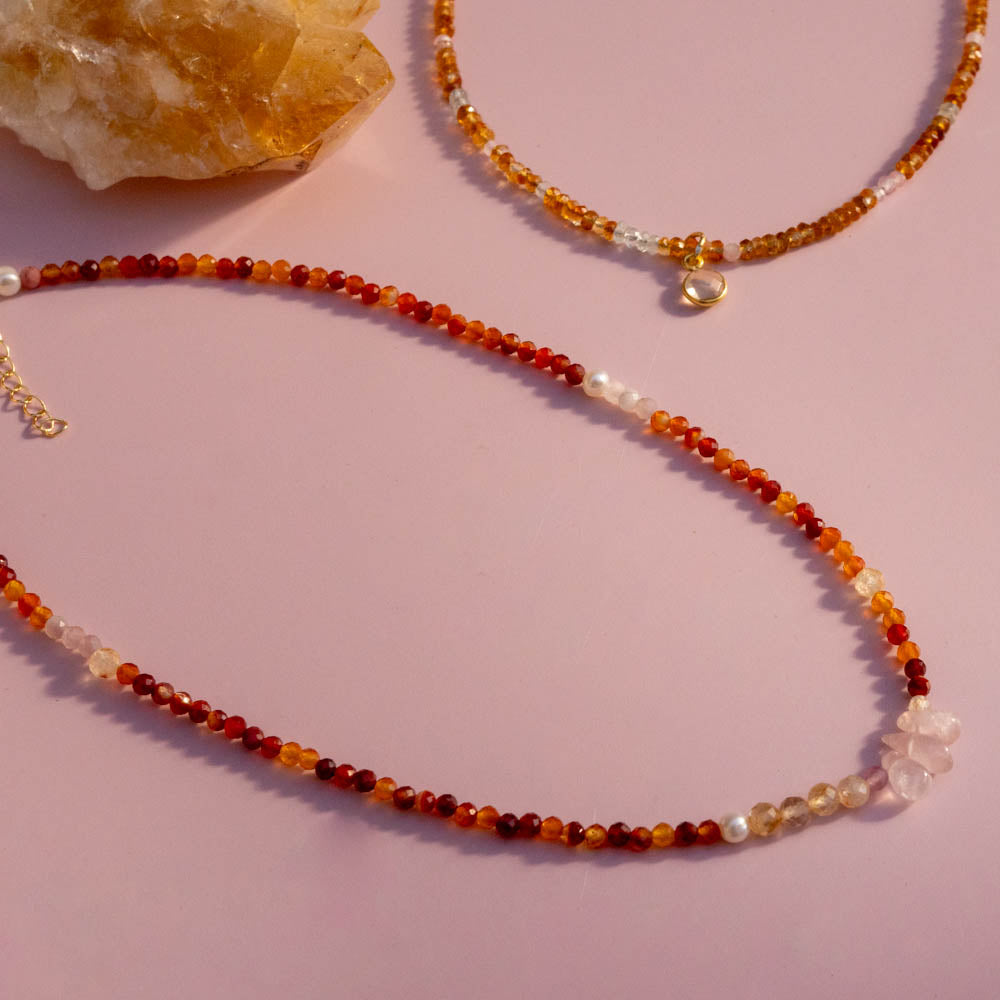 Beaded necklaces with red, orange, and white stones on a pink background